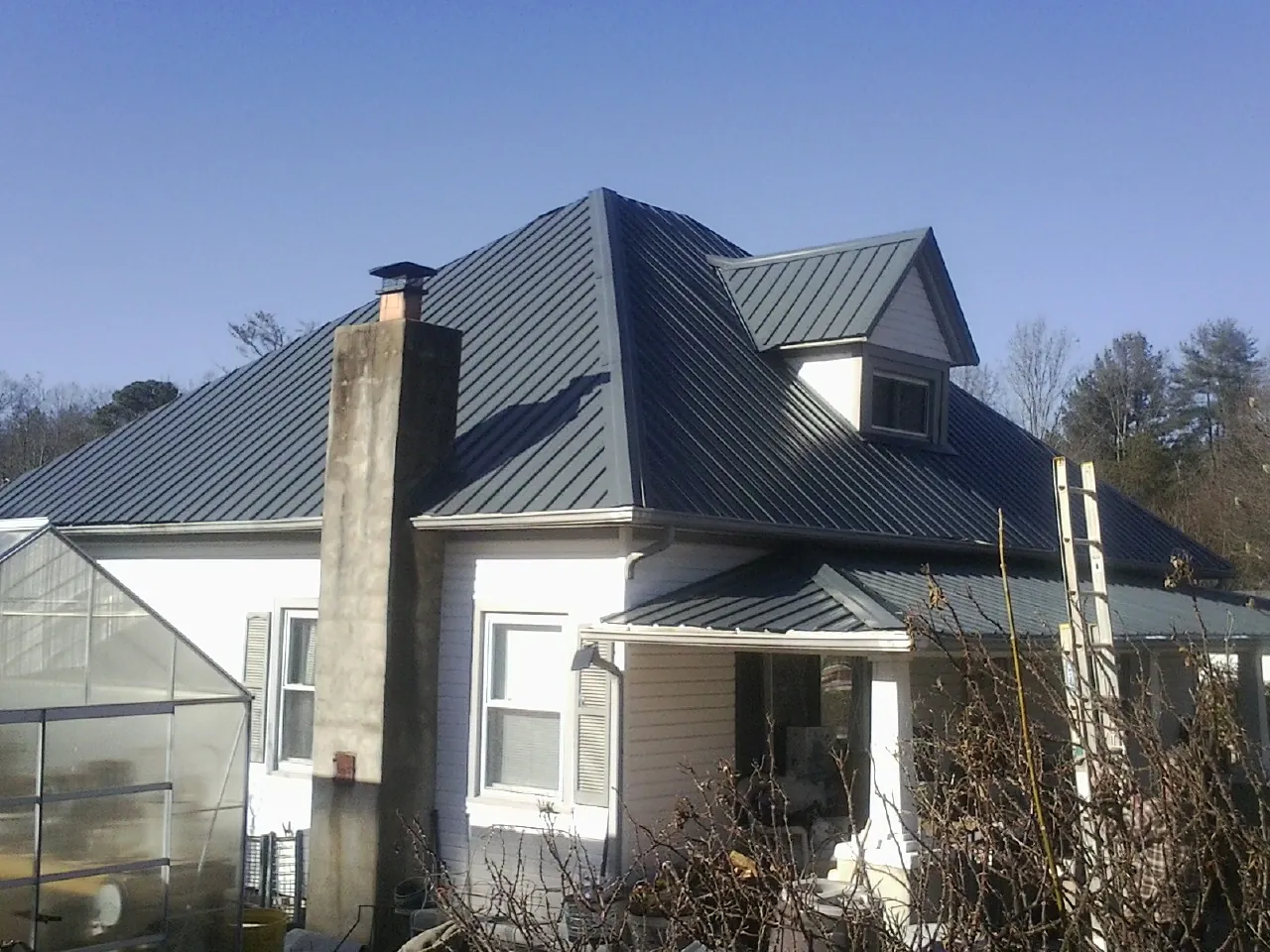 Dark blue standing seam metal roof on a white farmhouse with dormer — Slate & Tile Roof Repair by Roofing Brothers in Kerby
