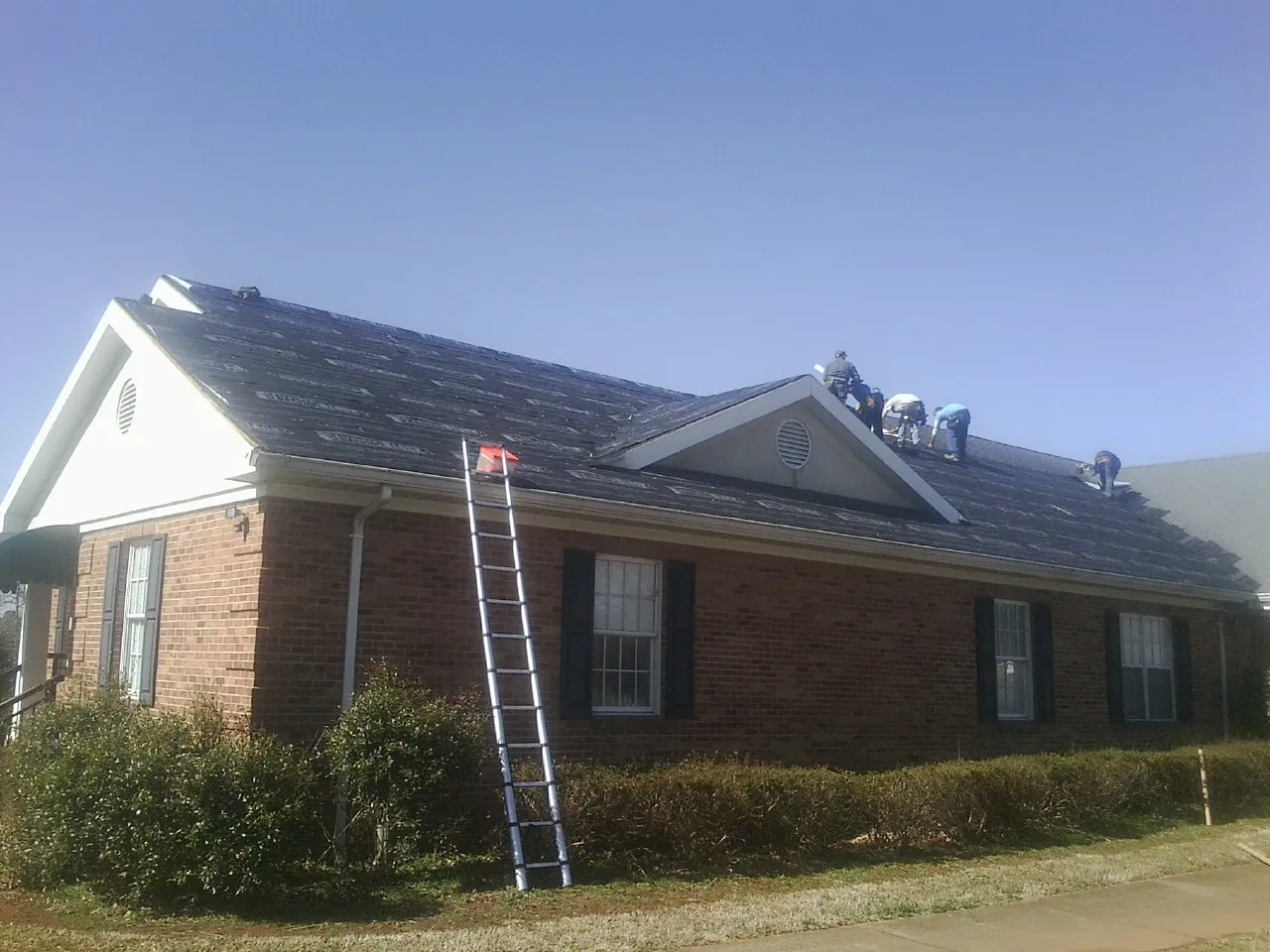 Crew tearing shingles off a brick ranch roof with a ladder set — Metal Roof Repair work by our crew in Kerby