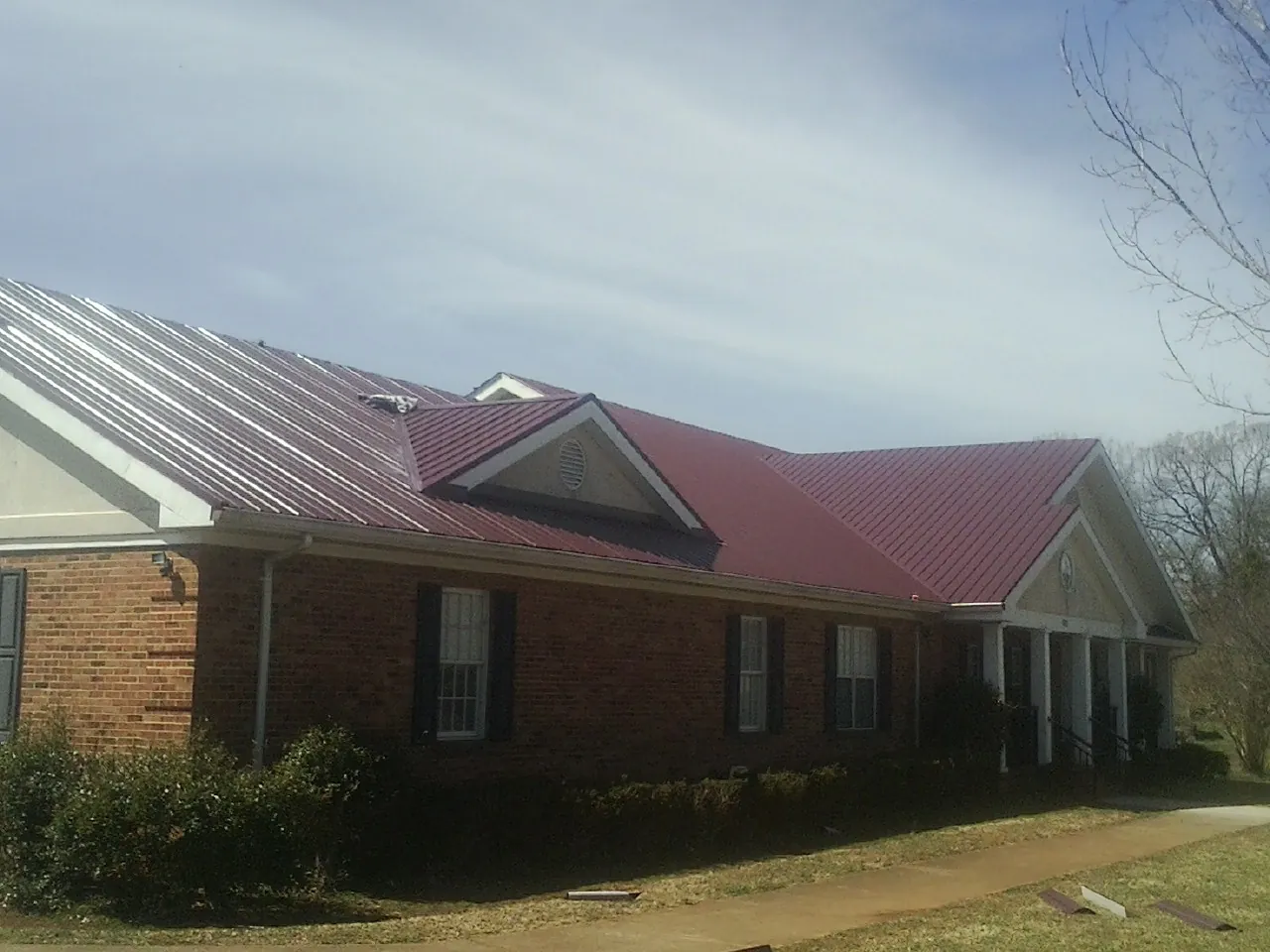 Red metal roof with gabled entries on a long brick building, from a Hail Damage Roof Repair job in Kerby