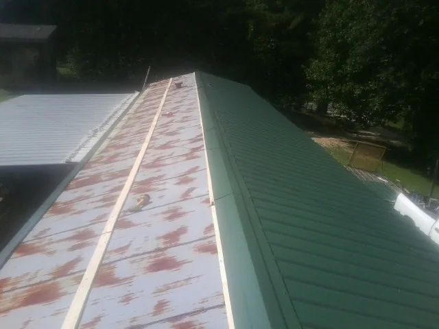 Old rusted panels beside newly installed green metal roofing — Wind Damage Roof Repair by Roofing Brothers in Kerby