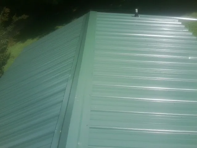 New green metal panels meeting at the ridge of a roof — Flat Roof Repair work by our crew in Kerby