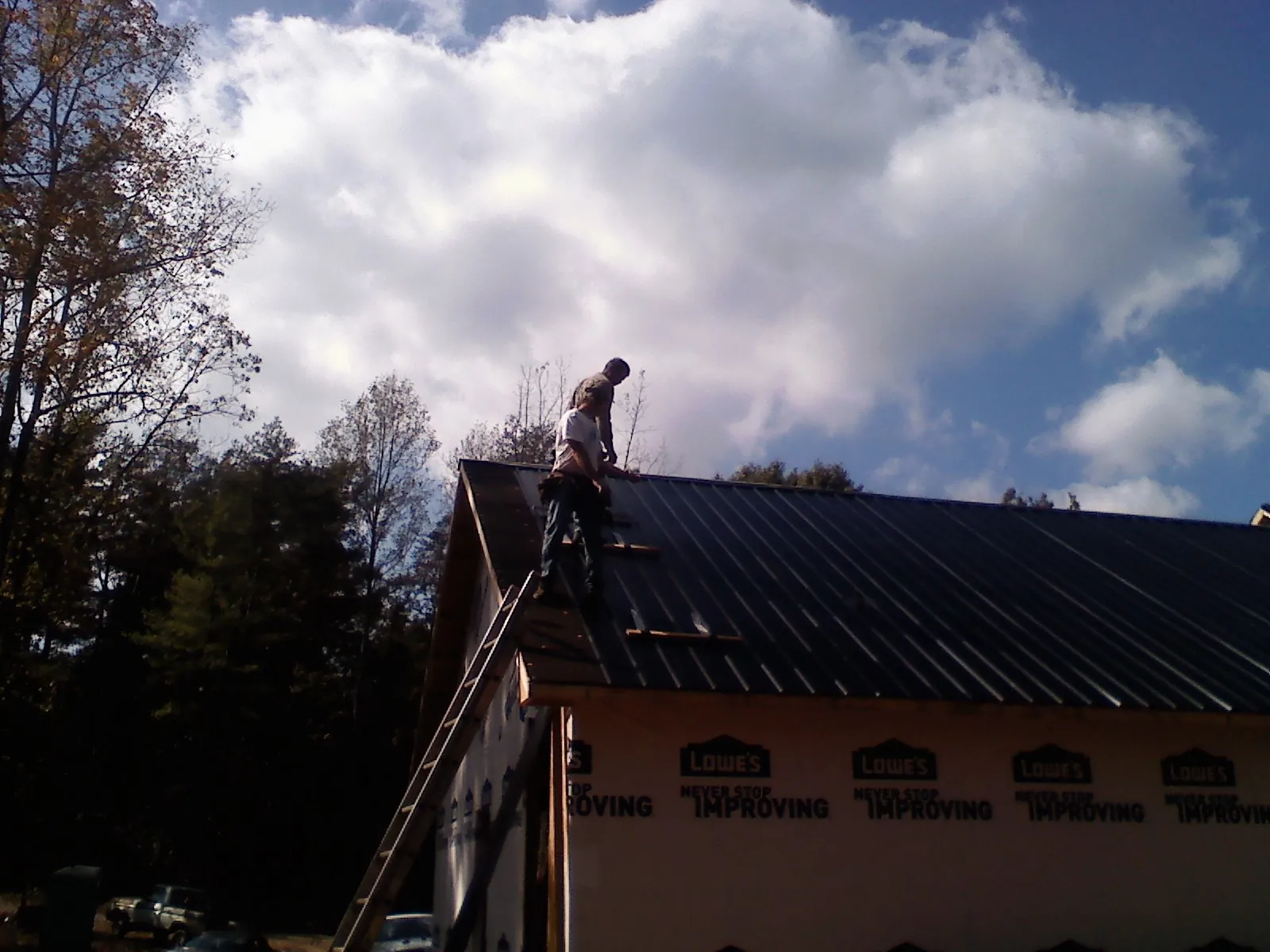 Roofer fastening dark metal panels high against a cloudy sky, from a Roof Inspection job in Kerby