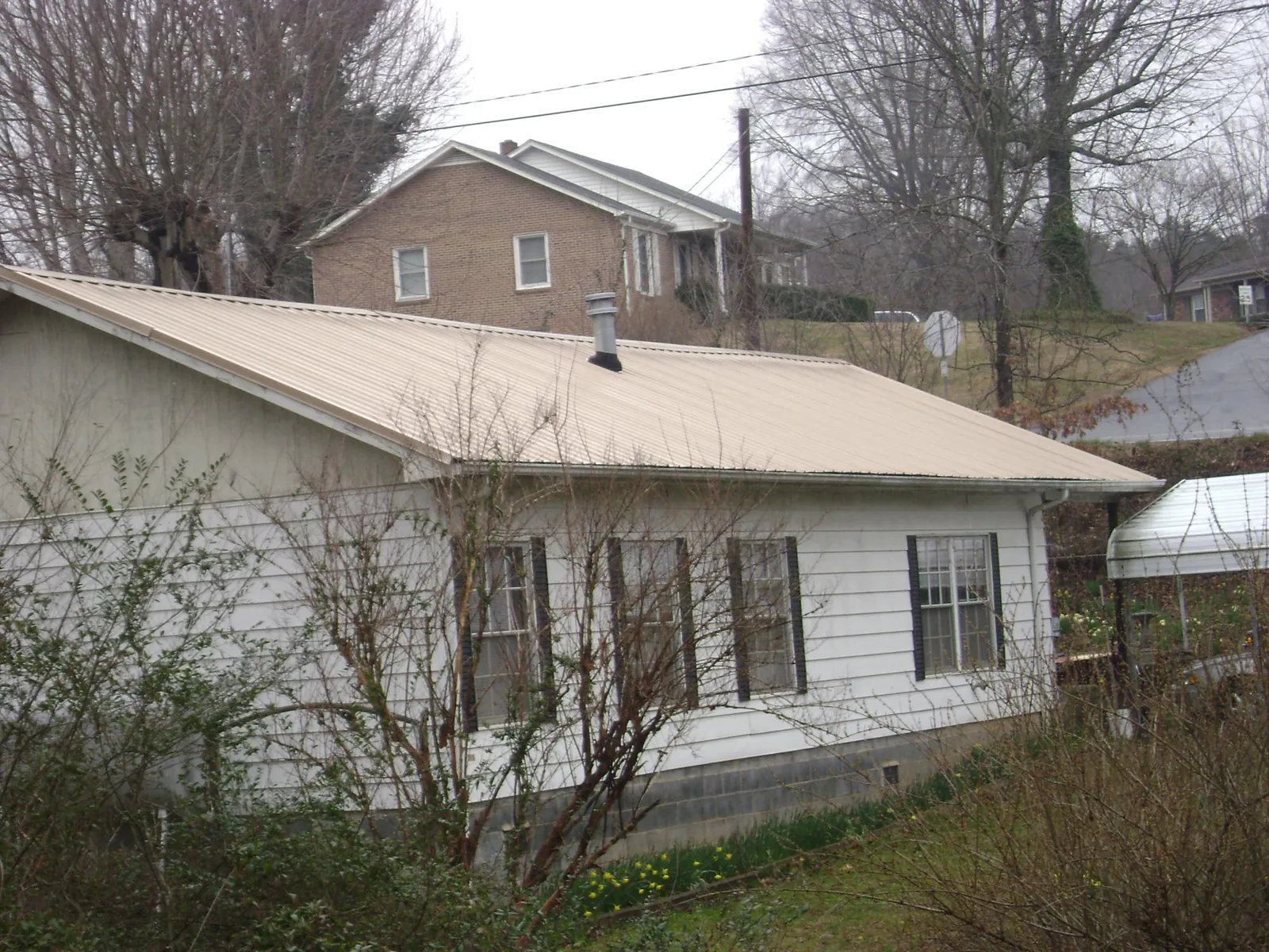 Tan metal roof on a white sided house set into a hillside — Commercial Roofing by Roofing Brothers in Kerby